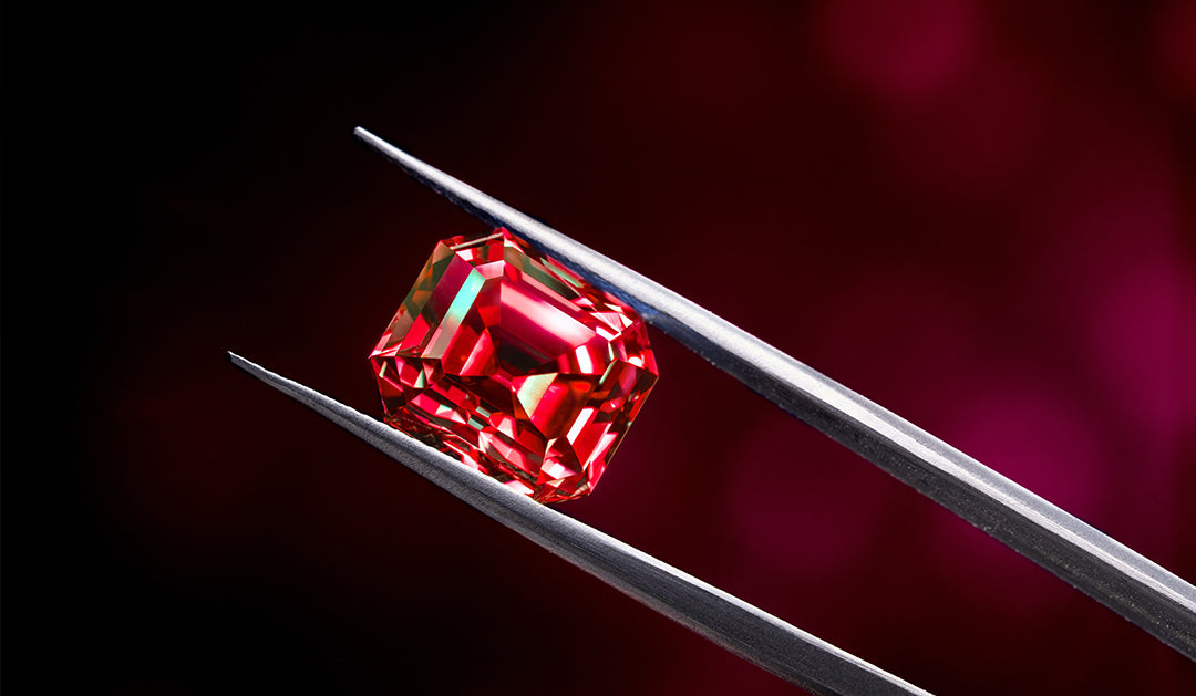 Red diamond being held with tweezers against a black gradient background