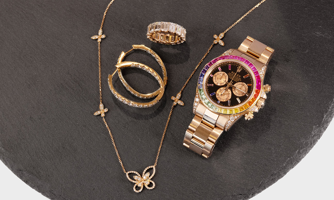 Gold Watch with Gold diamond hoops earrings a gold diamond ring and a gold diamond butterfly pendant necklace on a black tabletop
